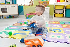 Adorable caucasian baby playing with truck toy sitting on floor at kindergarten