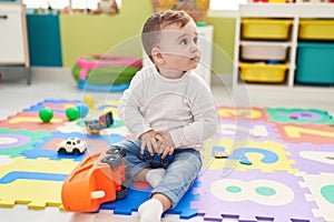 Adorable caucasian baby playing with truck toy sitting on floor at kindergarten