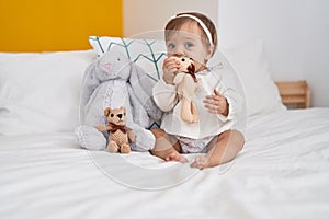 Adorable caucasian baby sitting on bed bitting doll at bedroom