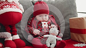 Adorable caucasian baby sitting on sofa with santa claus toy and christmas gift at home