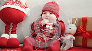 Adorable caucasian baby sitting on sofa with santa claus toy and christmas gift at home