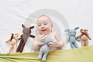 Adorable caucasian baby smiling confident lying on bed with dolls at bedroom
