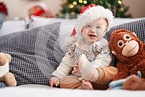 Adorable caucasian baby smiling confident sitting on sofa by christmas tree at home