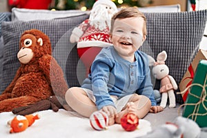 Adorable caucasian baby smiling confident sitting on sofa by christmas tree at home