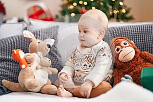 Adorable caucasian baby smiling confident sitting on sofa by christmas tree at home