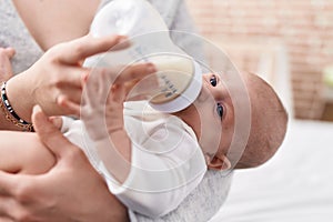 Adorable caucasian baby sucking feeding bottle at bedroom
