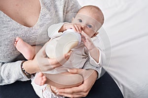 Adorable caucasian baby sucking feeding bottle at bedroom