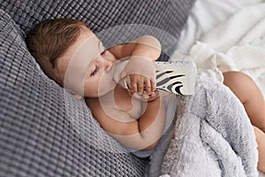 Adorable caucasian baby sucking milk on feeding bottle sitting on sofa at home