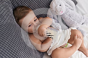 Adorable caucasian baby sucking milk on feeding bottle sitting on sofa at home