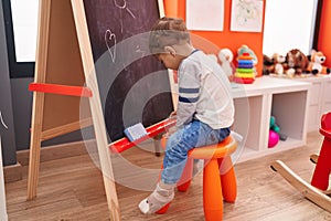 Adorable caucasian boy preschool student sitting on chair drawing on blackboard at kindergarten