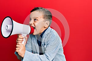 Adorable caucasian boy screaming using megaphone over isolated red background