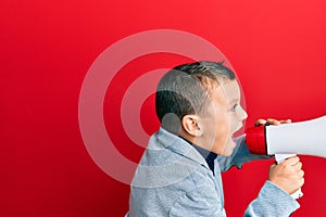 Adorable caucasian boy screaming using megaphone over isolated red background