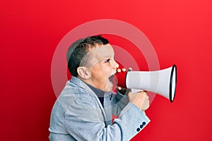 Adorable caucasian boy screaming using megaphone over isolated red background