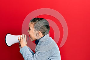 Adorable caucasian boy screaming using megaphone over isolated red background