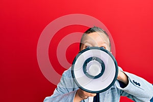 Adorable caucasian boy screaming using megaphone over isolated red background