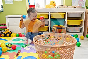 Adorable caucasian boy smiling confident playing with balls at kindergarten