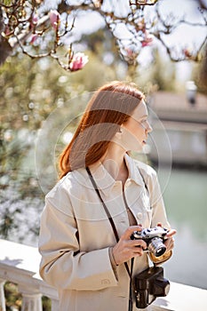 Adorable caucasian female in casual clothes walking in spring park alpne, with film camera