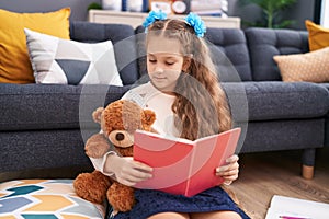 Adorable caucasian girl reading book sitting on floor at home