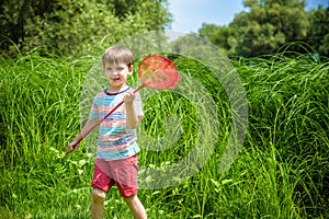 Adorable Caucasian kid playing with scoop-net on the meadow on warm and sunny summer or spring day.