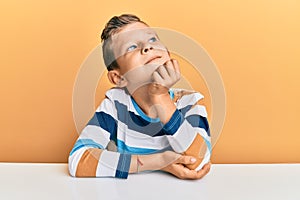 Adorable caucasian kid wearing casual clothes sitting on the table with hand on chin thinking about question, pensive expression