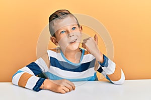 Adorable caucasian kid wearing casual clothes sitting on the table smiling with happy face looking and pointing to the side with