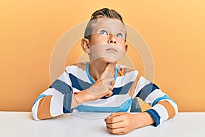 Adorable caucasian kid wearing casual clothes sitting on the table thinking concentrated about doubt with finger on chin and