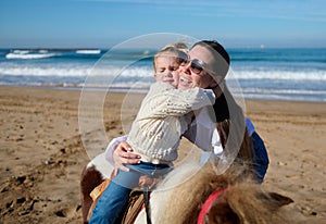 Adorable Caucasian little child girl hugging her mother while riding a horse on the beach