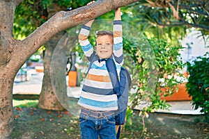 Adorable caucasian student boy smiling happy hanging on tree branch at the park