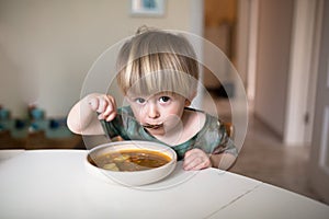 Adorable caucasian toddler boy eating healthy soup in the kitch