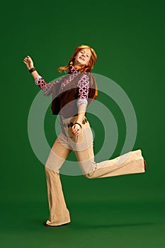 Adorable, charming girl, teenager with red hair dressed old-fashioned western style outfit posing against green studio