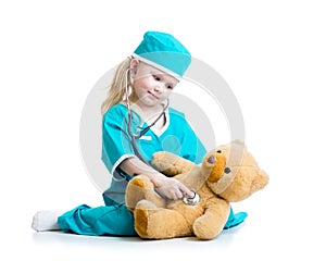 Adorable child with clothes of doctor examining teddy bear toy