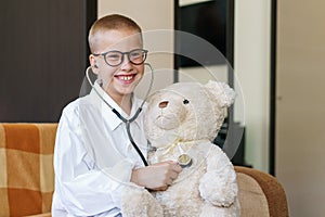 Adorable child, dressed as doctor, playing with a soft toy at home on couch.
