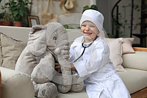 Adorable child dressed as doctor playing with toy elephant, checking its breath with stethoscope