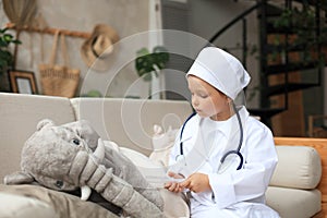 Adorable child dressed as doctor playing with toy elephant, checking its breath with stethoscope