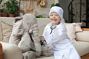 Adorable child dressed as doctor playing with toy elephant, checking its breath with stethoscope