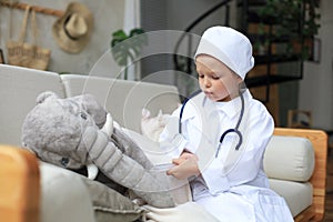 Adorable child dressed as doctor playing with toy elephant, checking its breath with stethoscope