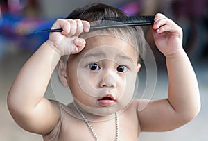 Adorable child girl with black eyes looking at the camera and holding a dirty comb up her head