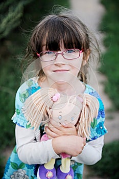 Adorable child girl in glasses hugs baby doll