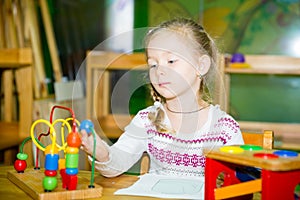 Adorable child girl playing with educational toys in nursery room. Kid in kindergarten in Montessori preschool class.