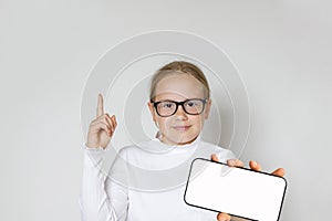 Adorable child girl with smartphone pointing up on white background. Kid holding cell phone with big blank empty white screen