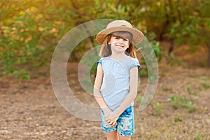Adorable child girl in straw hat spending time outdoor on summer day. Happy portrait of shy smiling kid