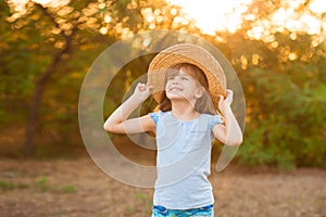 Adorable child girl in straw hat spending time outdoor on summer day. Happy portrait of shy smiling kid