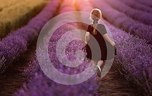 adorable child girl is walking in a field of lavender on sunset light. Kid in black dress is having fun on nature on
