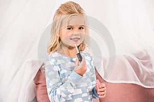 Adorable child holding lip gloss and looking photo