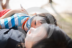 Adorable child hugs mother lying on beach hammock and acts like a baby