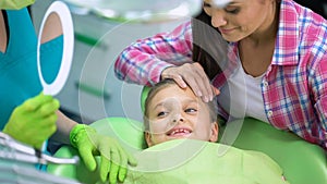 Adorable child smiling after dental procedures, watching healthy teeth in mirror