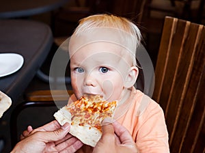 Adorable child toddler boy eating pizza slice at a restaurant summertime.