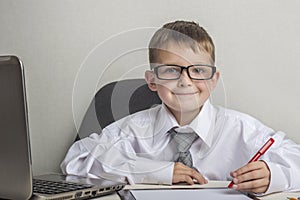 An adorable child is writing on a clipboard in suit and glasses. Little boss in the office. Children pretend to be adults