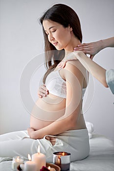 Adorable chinese pregnant female getting spa massage on back, hugging tummy