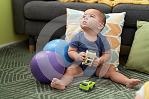 Adorable chinese toddler playing with cars toys sitting on floor at home